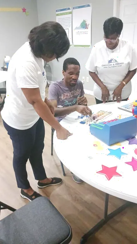 Staff guiding a participant through a hands-on sensory and learning activity at the table